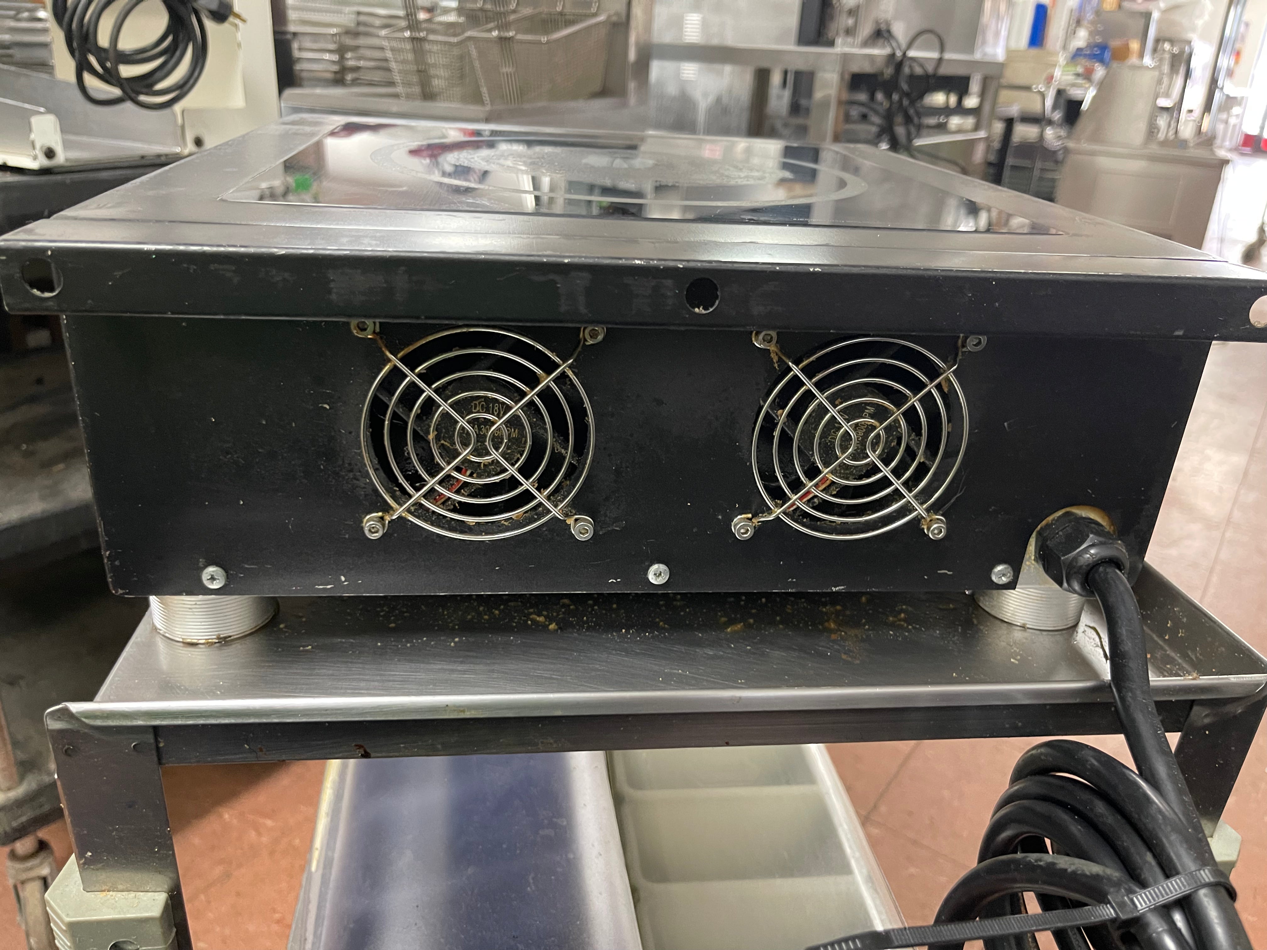 Back of a used Spring USA MAX Induction Cook and Hold Titanium Induction Range with visible scuffs and scratches, featuring a stainless steel body and a glass cooktop.