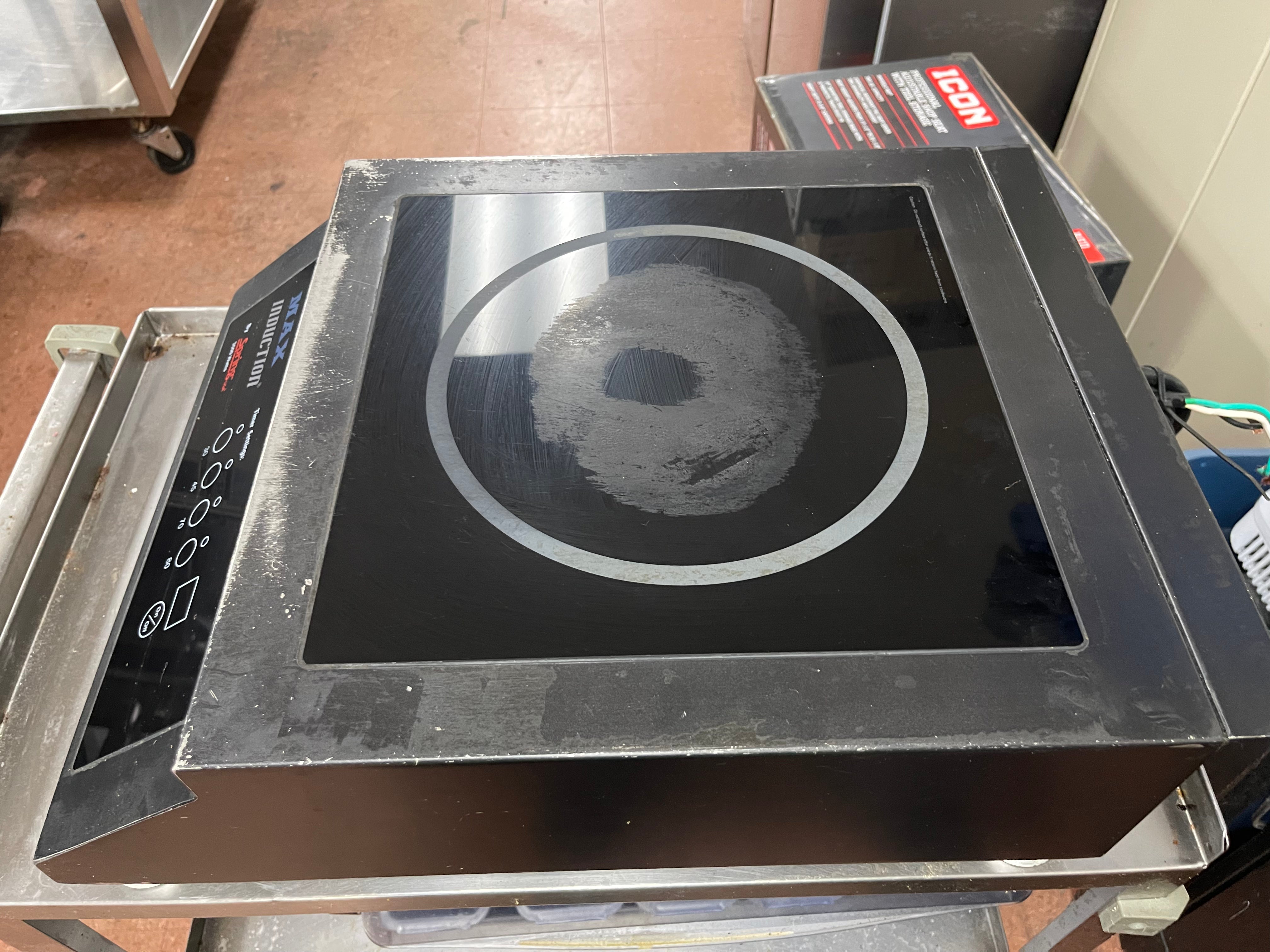 Top of a used Spring USA MAX Induction Cook and Hold Titanium Induction Range with visible scuffs and scratches, featuring a stainless steel body and a glass cooktop.