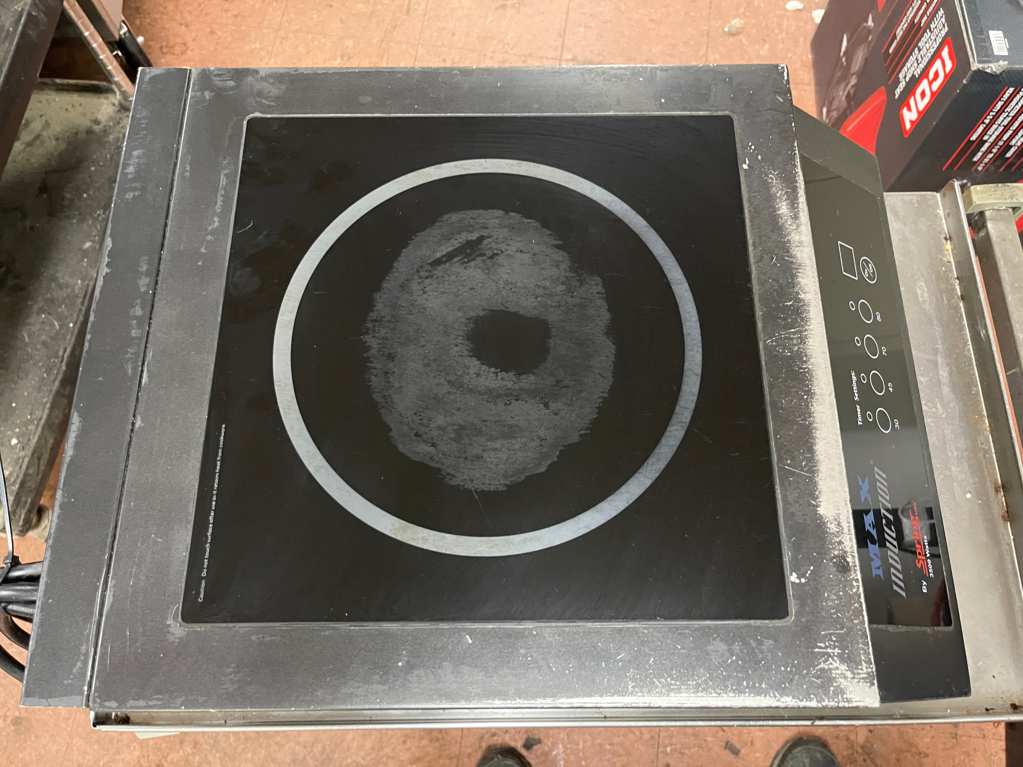 Top view of a used Spring USA MAX Induction Cook and Hold Titanium Induction Range with visible scuffs and scratches, featuring a stainless steel body and a glass cooktop.