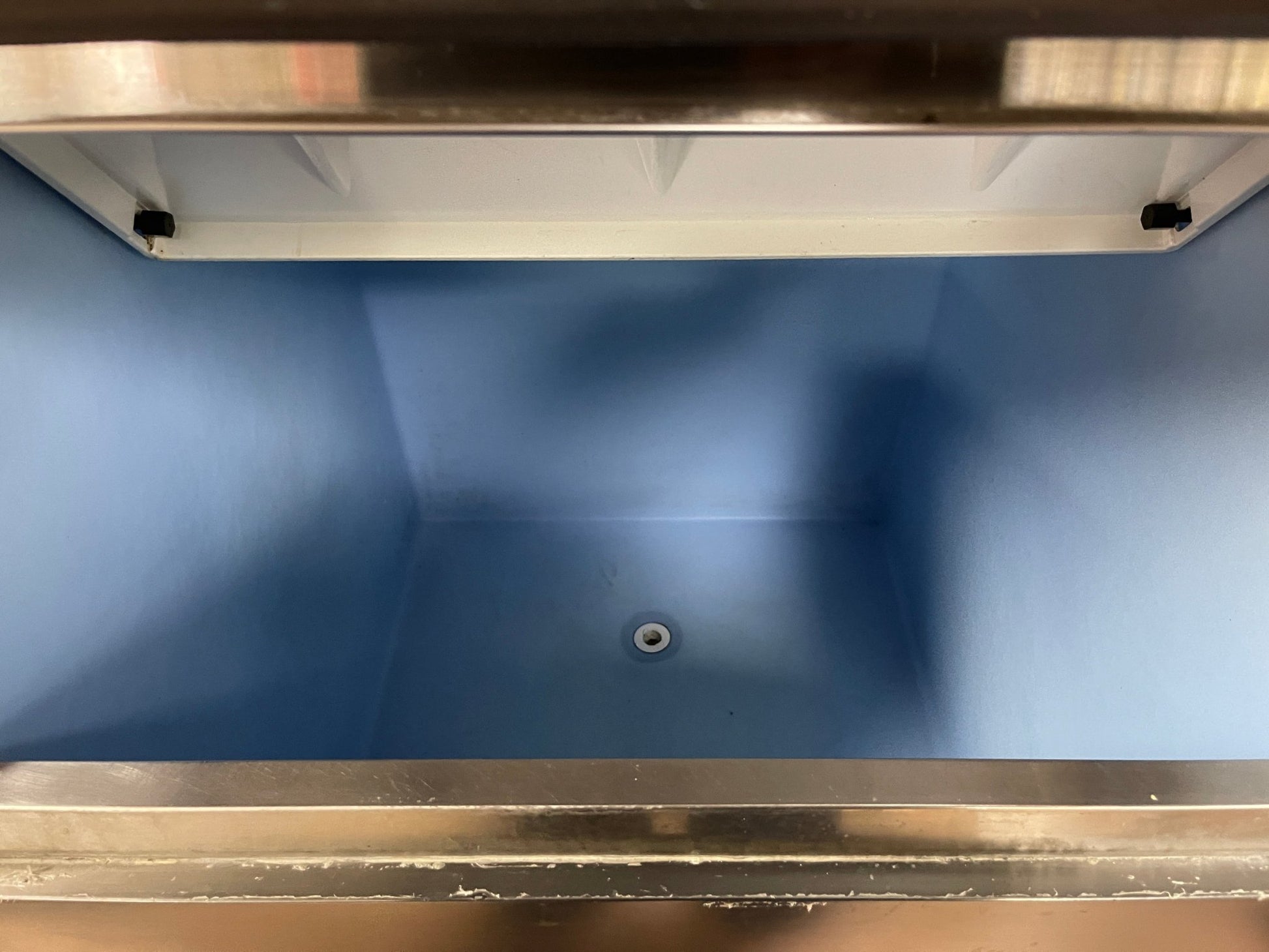 Inside compartment of ice maker bin that's blue with a white drain hole at bottom